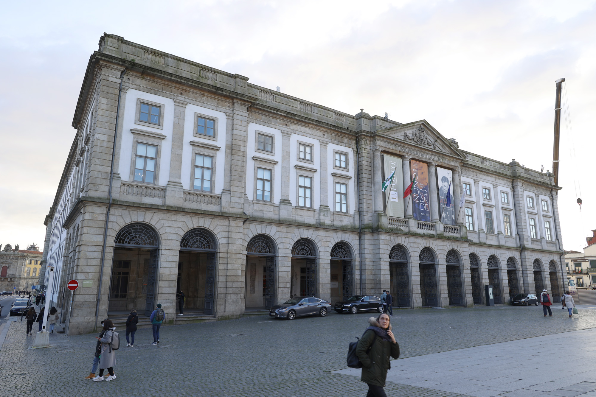 Vista da fachada do edifício da Reitoria da Universidade do Porto com algumas pessoas a passar na Praça dos Leões.