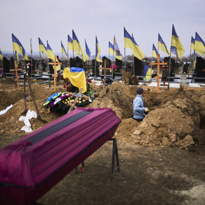 caixão junto a cova aberta no chão rodeada de bandeiras ucranianas
