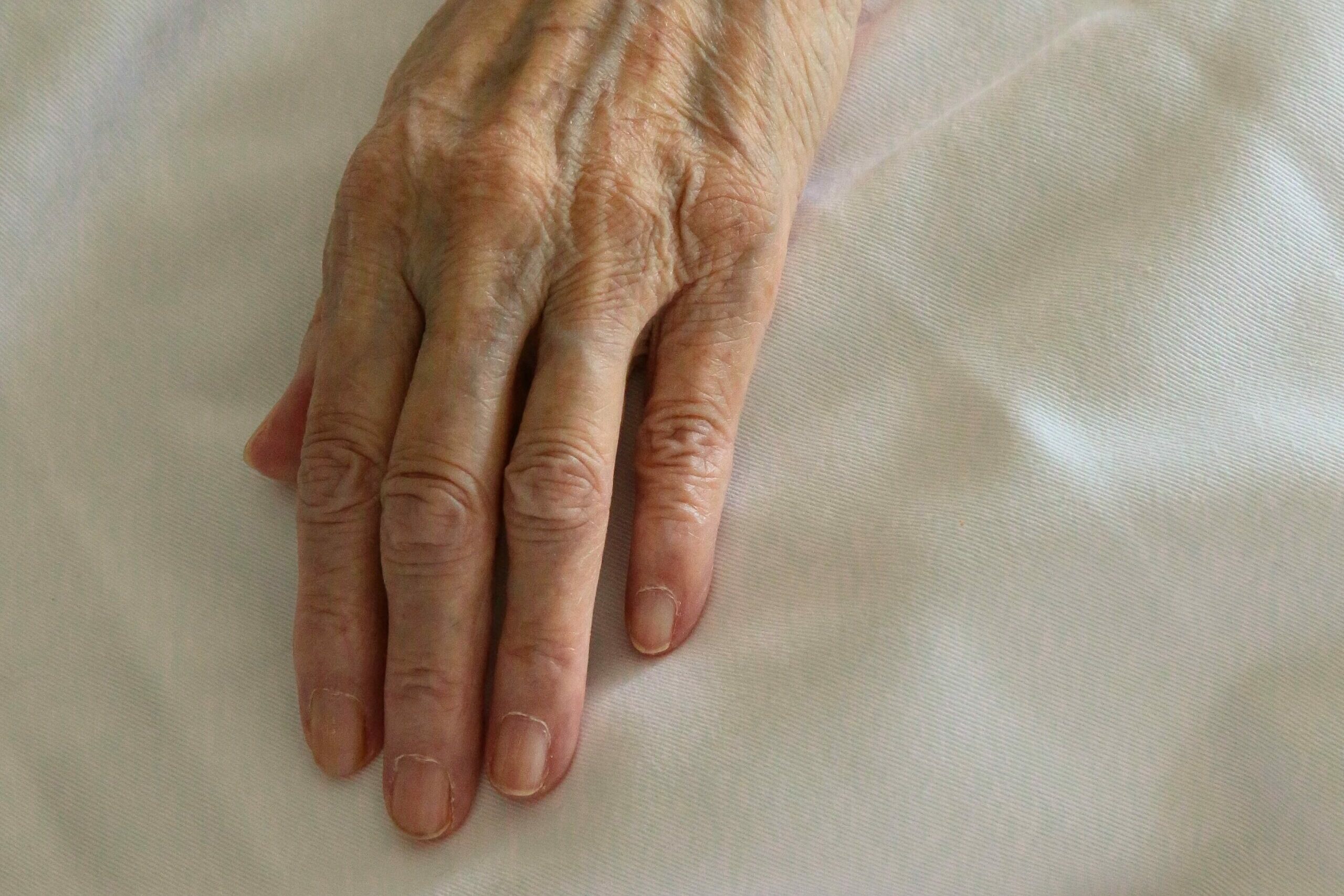 mão de idoso pousada sobre um lençol